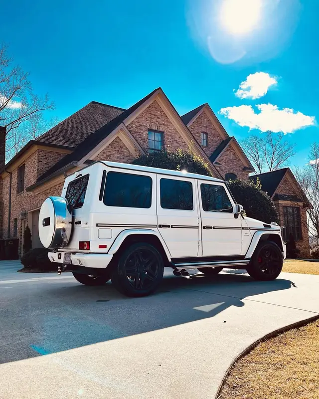 A white Mercedes G-Wagon gleaming in the driveway of a brick home under a blue sky