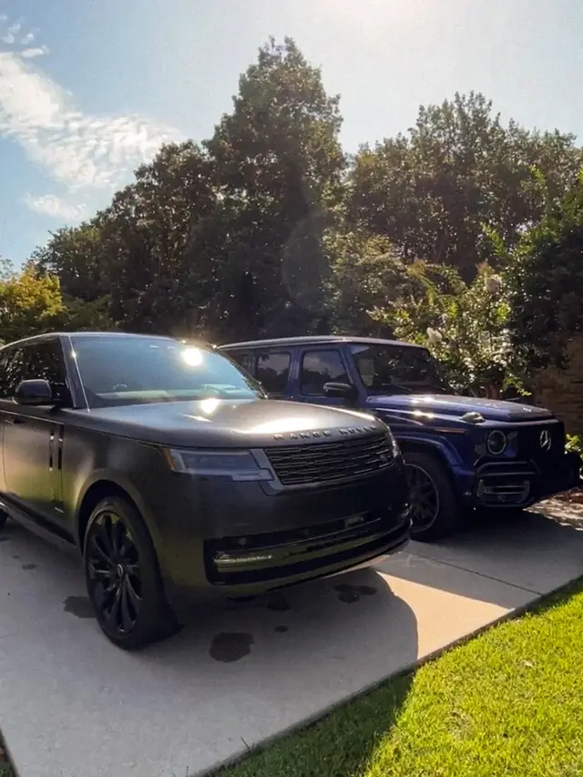 A matte black Range Rover and a blue G-Wagon side by side on a driveway in low sun after a detail