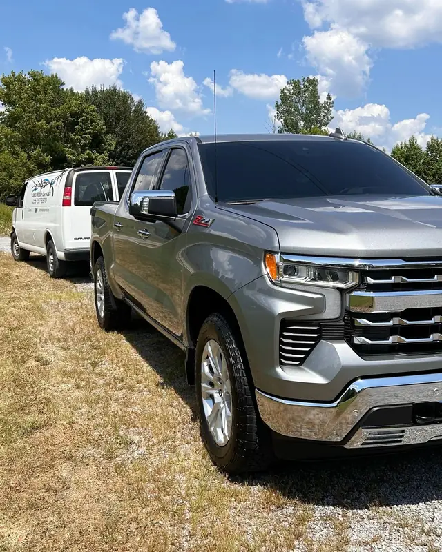 A freshly detailed grey Chevy Silverado 1500 on a lawn with the white BMC van parked behind it